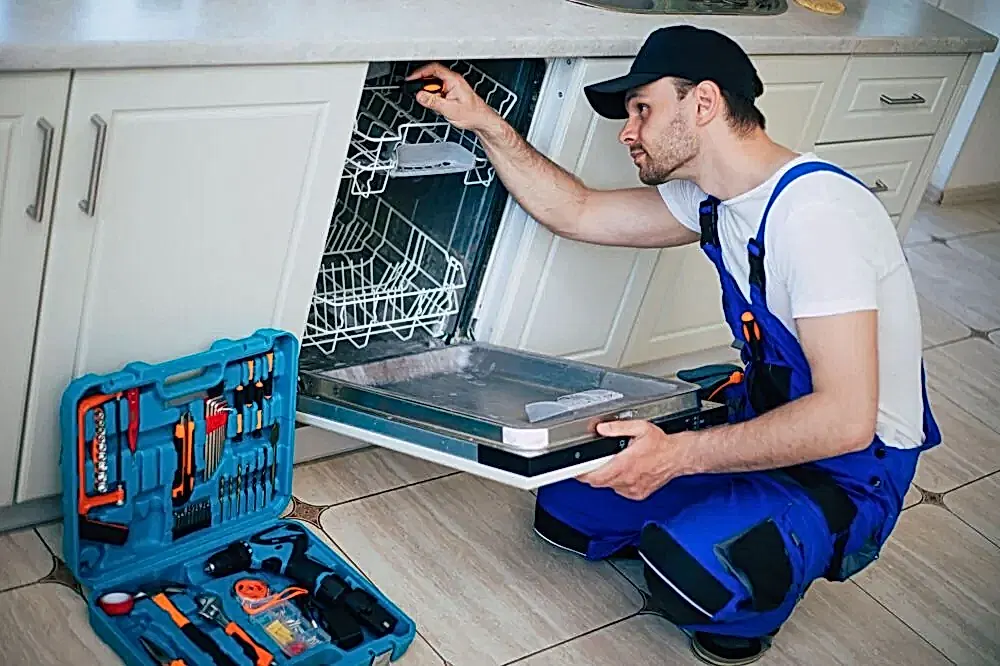 young-modern-serviceman-in-worker-suit-during-the-repairing-of-the-dishwasher-on-the-domestic-kitchen